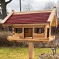 Preview: xxl-vogelhaus-groot-rote-bitumenschindeln-dunkelbraun-gebeizte-fensterlaeden-tueren-fensterzargen-boden-mit-zaun-im-garten