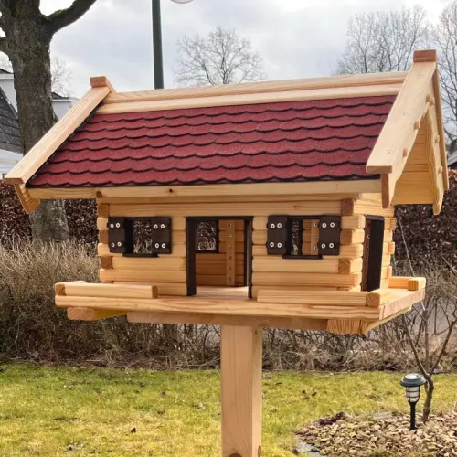 xxl-vogelhaus-groot-rote-bitumenschindeln-dunkelbraun-gebeizte-fensterlaeden-tueren-fensterzargen-boden-mit-zaun-im-garten